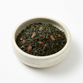Dry green tea leaves in a ceramic bowl on a white background